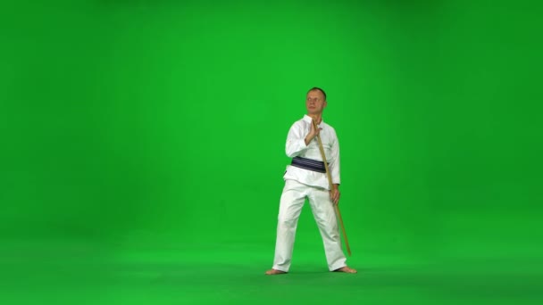 Męski mistrz Kendo na białym wojowniku kimono ćwiczący sztukę walki z bambusowym bokkenem na zielonym ekranie. — Wideo stockowe