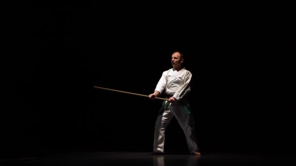 흰 기모노를 입고 검은 배경에서 대나무 주걱으로 무술을 연습하고 있는 켄 도 전투기. — 비디오