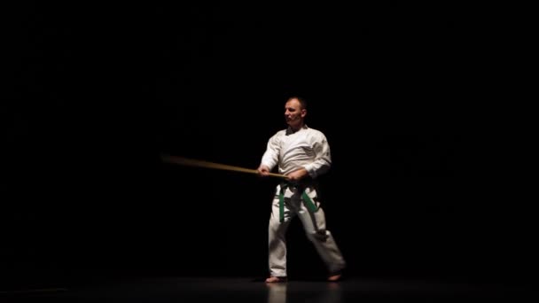 Kendo bojovník na bílém kimonu cvičí bojové umění s bambusovým bokken na černém pozadí. — Stock video