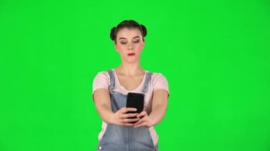 Genç bir kadın cep telefonuyla selfie çekiyor sonra da yeşil ekrana bakıyor.