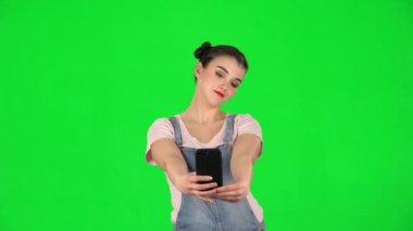 Kız cep telefonuyla selfie çekiyor sonra da yeşil ekrana bakıyor.