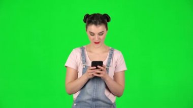 Genç gülümseyen kadın yeşil ekranda telefonuyla mesaj atıyor.