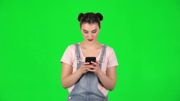 Young smiling woman texting on her phone on green screen — Stock Video