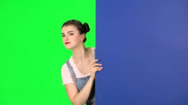 Mavi, boş bir levhanın arkasından dışarı bakıp kendini işaret eden Finge 'i çağıran kadın.