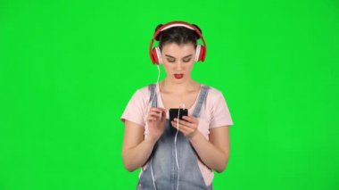 Büyük kırmızı kulaklıklı kız yeşil ekranda cep telefonundan müzik seçiyor.