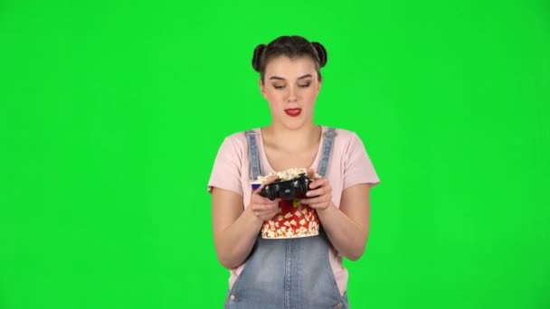Meisje speelt een videospel en kauwt popcorn op een groen scherm — Stockvideo