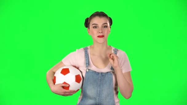 Junge Frau mit Fußballball, jubelt seiner Lieblingsmannschaft zu, während sie das Spiel auf der grünen Leinwand im Studio verfolgt. — Stockvideo