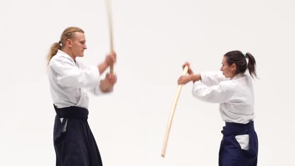 Man en vrouw oefenen aikido met bokken. Geïsoleerd op wit. Sluit maar af. Langzame beweging. — Stockvideo