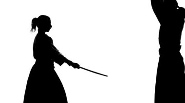 Keikogi ya da kimonolu siyah erkek ve kadın siluetleri bokken kullanarak aikido gösteriyorlar. İzole edilmiş. Ağır çekim. Kapat..