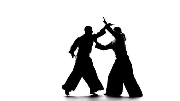 Black silhuettes of two males in keikogi or kimono showing aikido using tanto. Isolated, white. Slow motion. — Stock Video