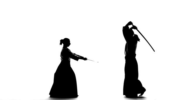 Black silhuettes of male and female in keikogi or kimono demonstrating aikido using bokken. Isolated. Slow motion. — Stock Video