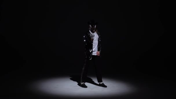 Mladý stylový muž tančící stylově Michael Jackson, reflektor na černém pozadí.