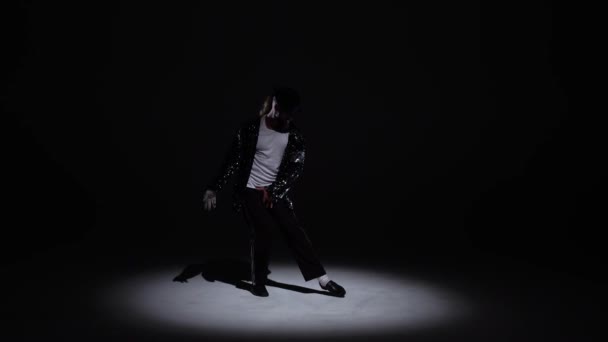 Молодий стильний чоловік танцює в стилі Майкла Джексона, прожектор на чорному фоні. — стокове відео