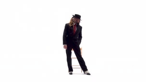 Un homme élégant avec un chapeau noir danse une danse érotique. Il utilise une chaise et une cigarette. Fond blanc . — Video