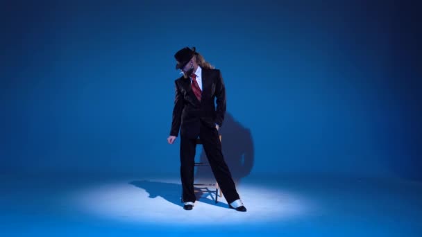 Elegant man i svart hatt dansar erotisk dans. spotlight på en blå bakgrund. — Stockvideo