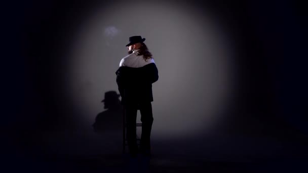 Elegante man met een zwarte hoed danst een erotische dans. Spotlight op een zwarte achtergrond. — Stockvideo
