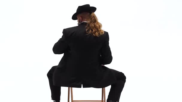 Un hombre elegante con un sombrero negro está bailando un baile erótico. Usa una silla y un cigarrillo. Fondo blanco. Primer plano, cámara lenta . — Vídeos de Stock