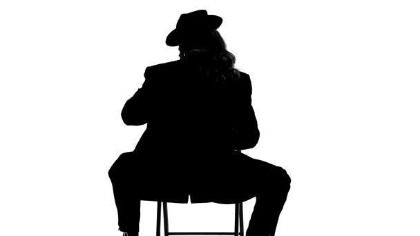 Silhouette Elegant man in a black hat is dancing an erotic dance. He uses a chair and a cigarette. White background. Close up, slow motion. — Stock Video