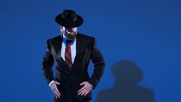 Elegante man met een zwarte hoed danst een erotische dans. Spotlight op een blauwe achtergrond. Close up, slow motion. — Stockvideo