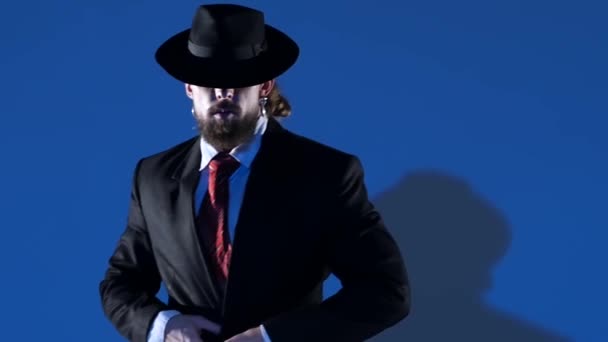 L'uomo elegante con un cappello nero sta ballando una danza erotica. Riflettori puntati su uno sfondo blu. Chiudi, rallenta. . — Video Stock