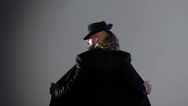 Un hombre elegante con un sombrero negro está bailando un baile erótico. Proyector sobre fondo negro. Primer plano, cámara lenta . — Vídeo de stock