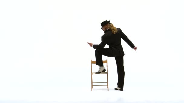 Az elegáns férfi fekete kalapban erotikus táncot jár. Egy széket és egy cigarettát használ. Fehér háttér. Bezárás, lassított felvétel.. — Stock videók