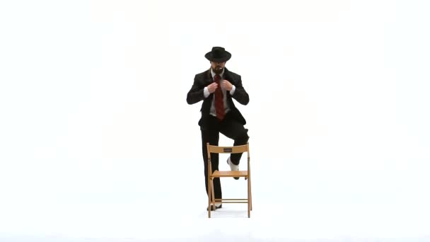 Um homem elegante de chapéu preto está a dançar uma dança erótica. Ele usa uma cadeira e um cigarro. Fundo branco. Fecha, câmara lenta. . — Vídeo de Stock