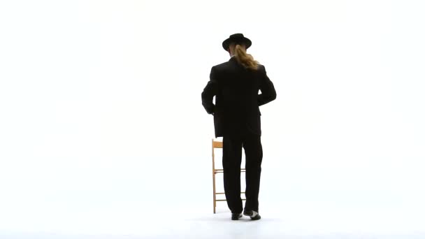 Elegant man i svart hatt dansar erotisk dans. Han använder en stol och en cigarett. Vit bakgrund. Närbild, slow motion. — Stockvideo