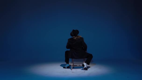 Elegant man in a black hat is dancing an erotic dance. Spotlight on a blue background. Close up, slow motion. — Stock Video