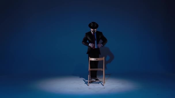 Un hombre elegante con un sombrero negro está bailando un baile erótico. Proyector sobre fondo azul. Primer plano, cámara lenta . — Vídeos de Stock