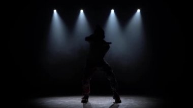 Siluetçi adam karanlık stüdyoda modern hip hop dansı yapıyor. Duman, ışık, kıvrım ve dönüşle..