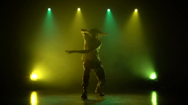 El hombre disfrutando del hip hop se mueve en un estudio oscuro con humo. Iluminación verde y amarillo. Silueta . — Vídeos de Stock