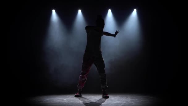 Человек наслаждается хип-хоп движениями в темной студии с дымом и освещением . — стоковое видео