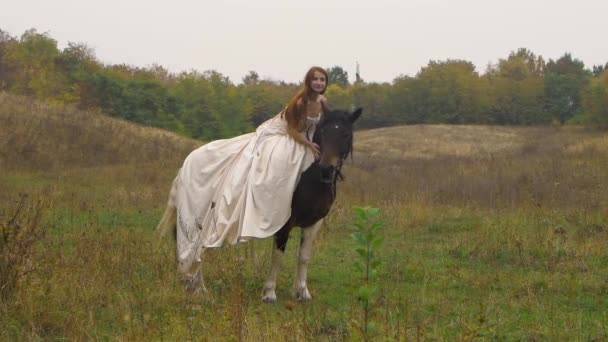 Vörös hajú, buzi ruhás lovas nő lovagol a pályán. — Stock videók