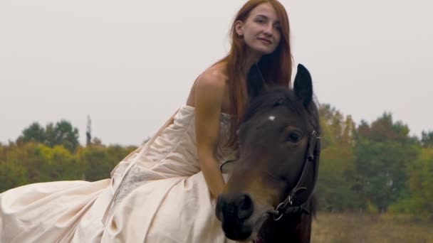 Імбир конячка в пухнастій сукні верхи на коні на лузі. Крупним планом — стокове відео