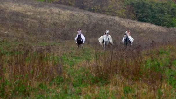 Tre donne in abiti bianchi stanno cavalcando cavalli attraverso la valle — Video Stock