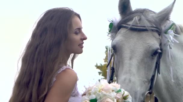 Hosszú hajú menyasszony fehér menyasszonyi ruhában pózol ló mellett. — Stock videók