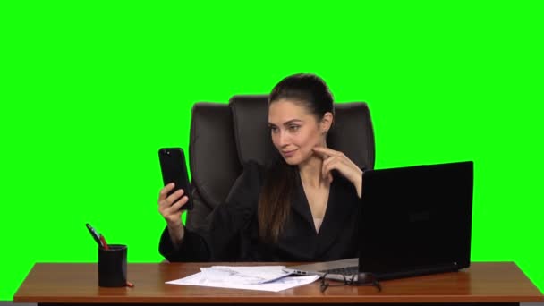 Mulher de negócios no local de trabalho tira uma selfie em seu telefone celular, em seguida, alegremente olha para a foto. Tela verde. Estúdio. Movimento lento — Vídeo de Stock