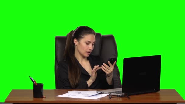 Frau am Arbeitsplatz betrachtet freudig das Foto auf ihrem Handy. Green Screen. Studio. Zeitlupe — Stockvideo