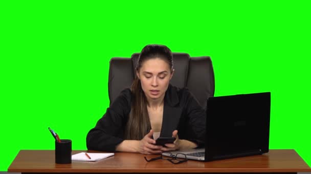 Business woman sitting at a desk writes a message on a cell phone with rage. Green screen. Studio. Slow motion — ストック動画