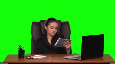 İşçi kız bir iş yerinde oturur deri koltuğa yaslanır ve tabletle iletişim kurar ve üzülür. Yeşil ekran. Yavaş çekim