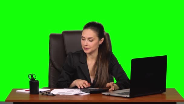 A mulher de negócios trabalha em um laptop, compara dados com uma calculadora e faz entradas em documentos. Tela verde. Movimento lento — Vídeo de Stock