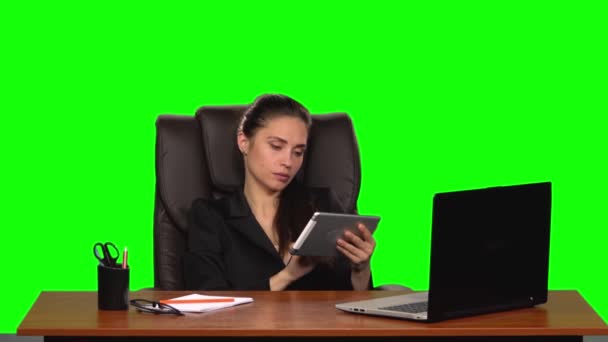 Arbetstagarflickan sitter på en arbetsplats lutande sig tillbaka i en läderstol och kommunicerar på en surfplatta och arg. Grön skärm. Långsamma rörelser — Stockvideo