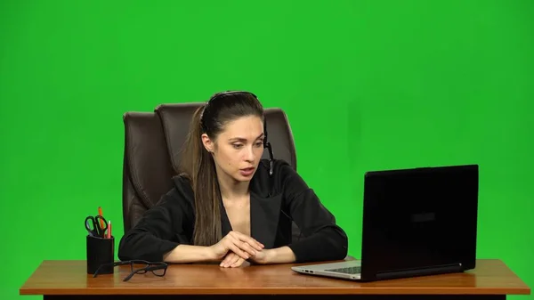 Business woman in headphones speaking by webcam and look at laptop. Green screen. Slow motion