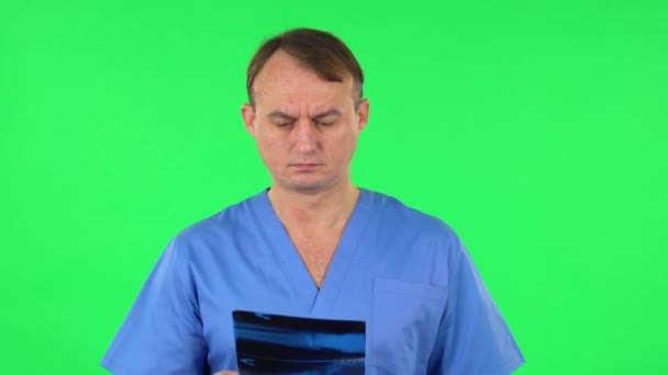 Médico varón con abrigo azul revisando rayos X apuntando a la instantánea. Pantalla verde — Vídeo de stock