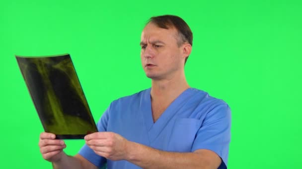 Мужчина-врач в синем пальто рассматривает рентген, указывая на снимок, объясняет и показывает большой палец, как. Зеленый экран — стоковое видео