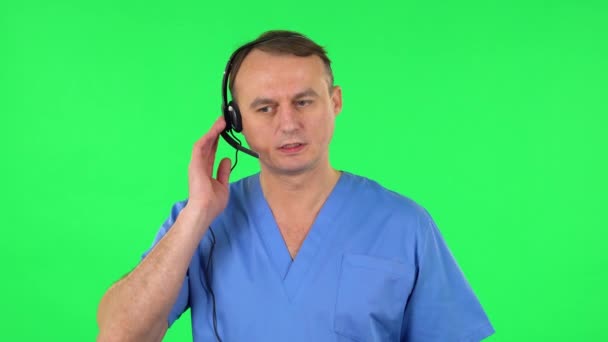 Ιατρικός μιλάει με ακουστικά στην υπηρεσία υποστήριξης. Πράσινη οθόνη — Αρχείο Βίντεο