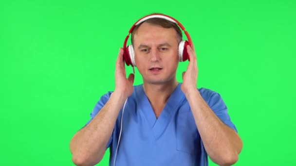 Hombre médico bailando y cantando con grandes auriculares rojos. Pantalla verde — Vídeos de Stock