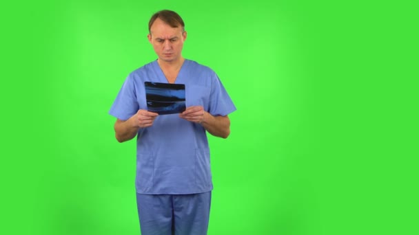 Mužský doktor v modrém plášti zkoumá rentgen ukazující na snímek. Zelená obrazovka — Stock video