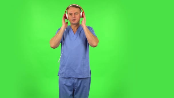 Hombre médico bailando y cantando con grandes auriculares rojos. Pantalla verde — Vídeos de Stock